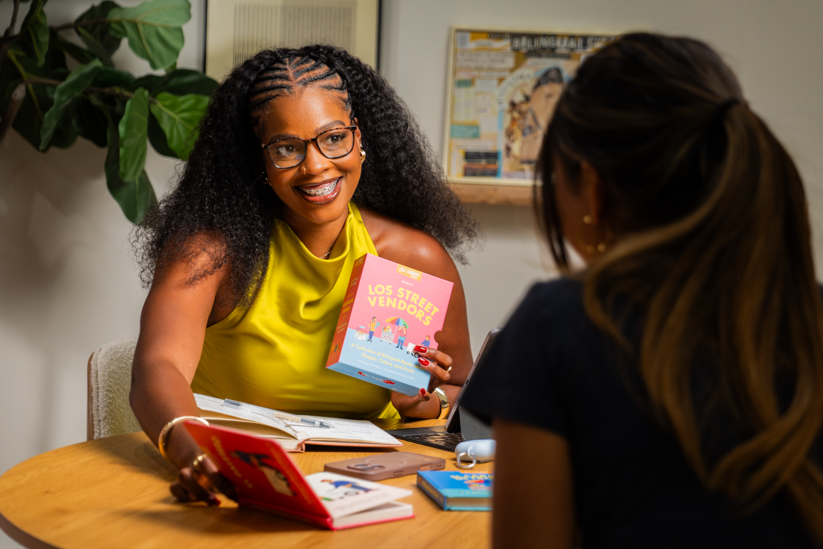 Kylah in session across the table from a client, holding up a bilingual picture book while they read together